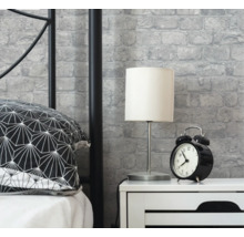 Schlafzimmerszene mit Bett, Nachttisch, Lampe, Wecker und Mauerwerkstapete