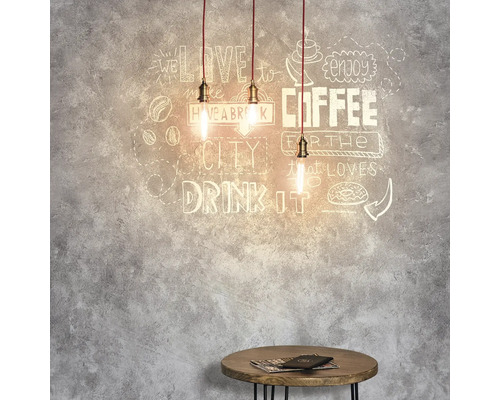 Drei Pendelleuchten über einem kleinen Tisch vor einer Wand mit Kaffeemotiven