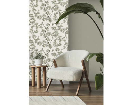 Szene mit floraler Tapete, Sessel, Beistelltisch, Teppich und Zimmerpflanze.