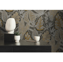 Dekoratives Interieur mit gemusterter Tapete mit floralen Elementen, einer Skulptur, einer Topfpflanze, einer Schale und einem Bleistift auf einer Kommode.