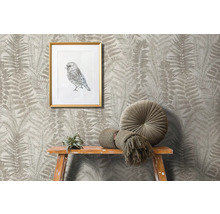 Szene mit Farnmuster-Tapete, gerahmtem Vogelbild, rundem Kissen und Dekoration auf einem Holzhocker