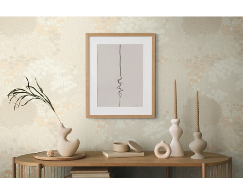 Scène décorative avec une image encadrée, des vases et des bougies sur une table en bois devant un papier peint à motifs.