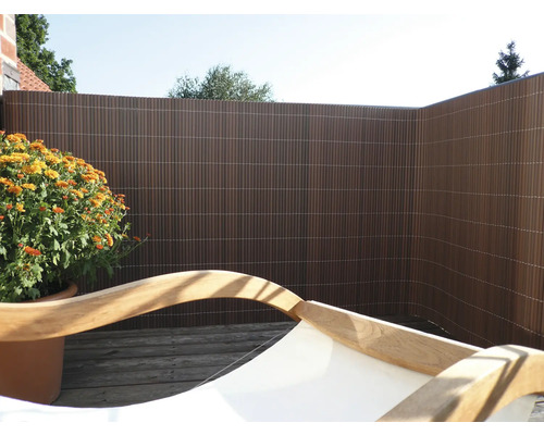 Terrasse mit Sichtschutzzaun aus Kunststoff, Holzliege und Pflanztopf mit Blumen