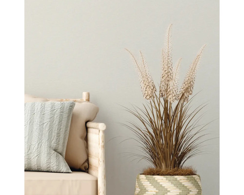 Dekorative Kunstpflanze im Korb neben einem Sofa mit Kissen