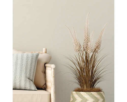 Dekorative Kunstpflanze im gewebten Korb neben einem Sofa mit Kissen.