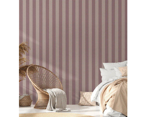 Schlafzimmer mit gestreifter Tapete, Korbsessel und Bett.