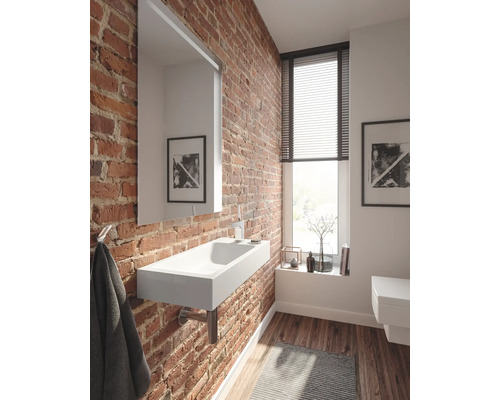 Salle de bains avec mur en briques, lavabo, miroir et fenêtre avec stores.