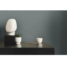 Dekorative Szene mit Skulptur, Pflanze und Tasse auf einer dunklen Holzkommode vor einer einfarbigen Wand.
