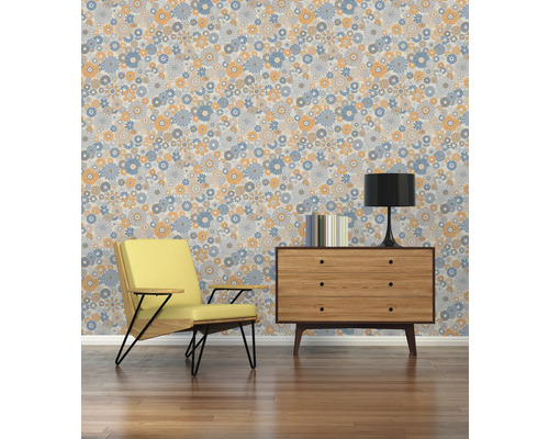 Intérieur avec fauteuil, commode, lampe, livres et papier peint à motifs floraux.