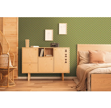 Zimmer mit grüner Tapete mit geometrischem Muster, Holzschrank, Bett und Korbstuhl.