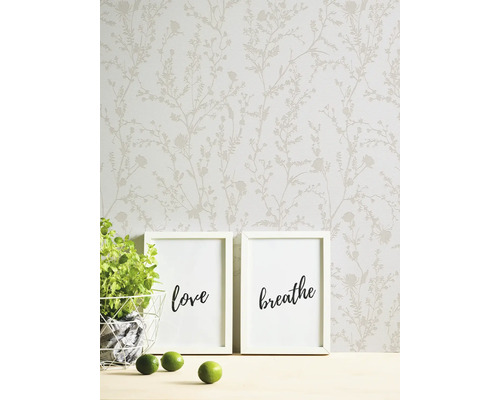 Papier peint à motif floral en arrière-plan, deux cadres photo avec les mots amour et respirer, plante en pot et citrons verts au premier plan.