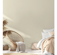 Helles Schlafzimmer mit Rattansessel, Bett und dekorativen Textilien für ein gemütliches Ambiente