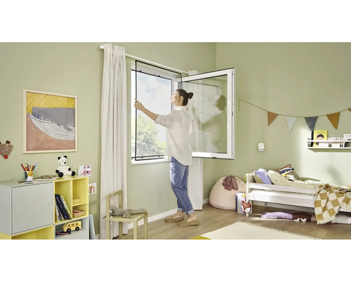 Une femme installe une moustiquaire sur la fenêtre d''une chambre d''enfant