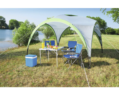 Scène de camping avec tonnelle, table, chaises et glacière sur une pelouse au bord d''un lac