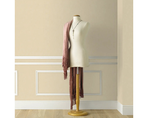 Schneiderpuppe mit Schal und Halskette vor einer Wand mit Zierleisten