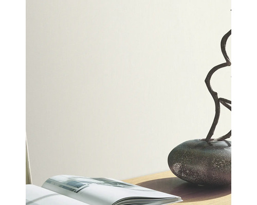 Mur clair avec vase, branches et livre sur une table.