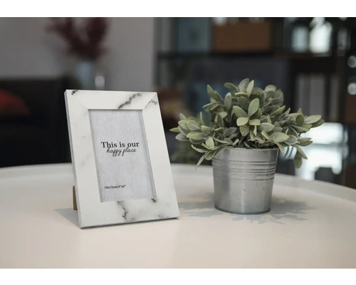 Dekorativer Fotorahmen aus Marmorimitat neben Topfpflanze