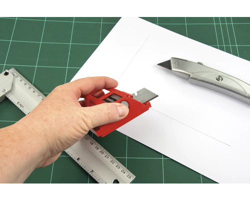 Hand mit Schneidwerkzeug, Lineal und Cutter auf Schneideunterlage