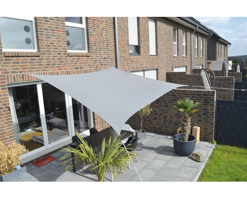 Voile d''ombrage grise au-dessus d''une terrasse avec table et plantes.