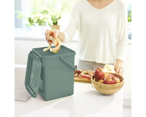 Une femme jette des restes de pommes dans un composteur dans la cuisine.