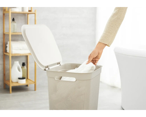 Wäschekorb mit Deckel im Badezimmer mit Person, die ein Handtuch hineinlegt.