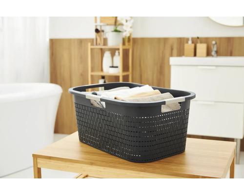 Dunkelgrauer Wäschekorb auf einem Holztisch in einem hellen Badezimmer.