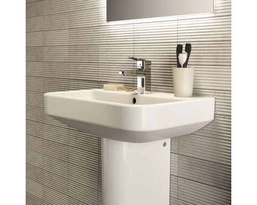 Lavabo avec colonne, robinet, savon, gobelet à brosse à dents et carrelage ondulé dans la salle de bain