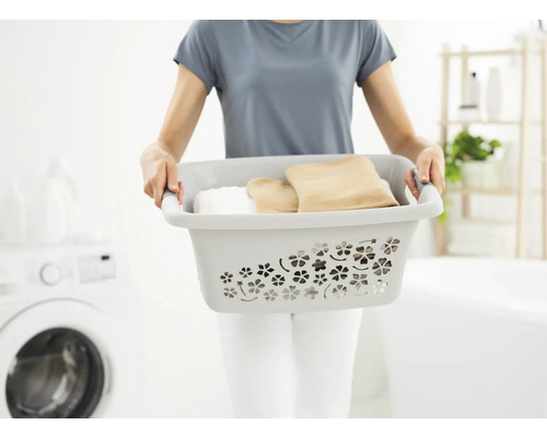 Frau trägt Wäschekorb mit Kleidung im Badezimmer