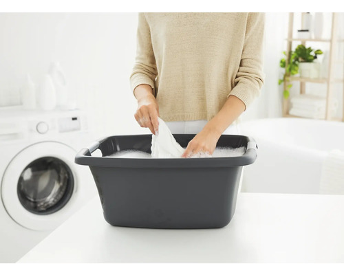 Frau wäscht Wäsche in einer Wäschewanne in einem hellen Badezimmer mit Waschmaschine