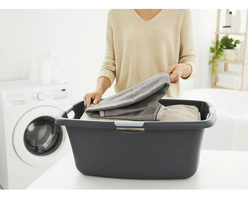 Frau legt Wäsche in einen grauen Wäschekorb im Waschraum.