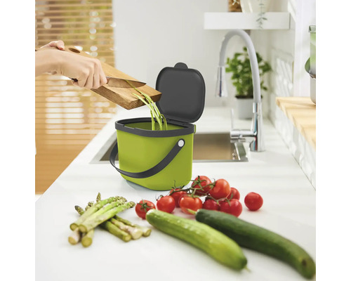 Scène d''une cuisine avec un seau à déchets organiques vert, une personne jetant des déchets de légumes, des tomates, des concombres et des asperges