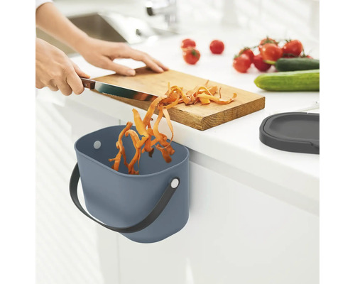 Une personne coupe des légumes et les jette dans une poubelle dans la cuisine.