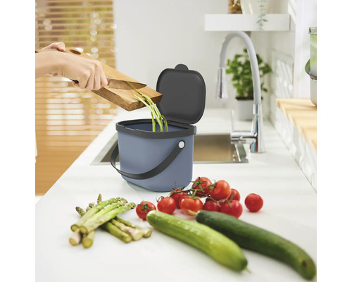 Une personne jette des déchets de légumes dans un seau à compost dans la cuisine.