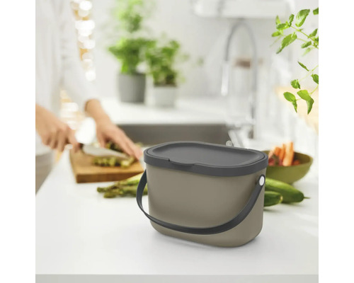 Poubelle avec couvercle et poignée sur table de cuisine, personne coupant des légumes