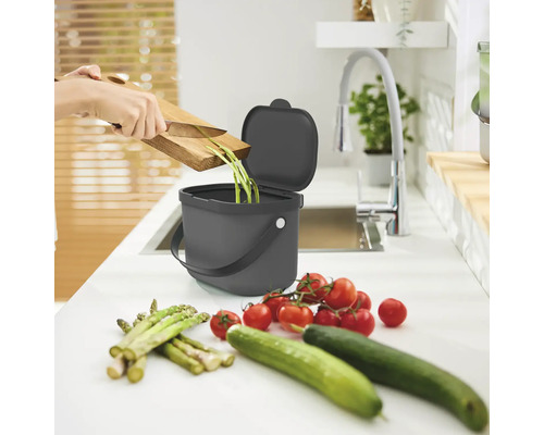 Scène de cuisine avec poubelle à compost, restes de légumes, planche à découper, couteau, tomates, concombres et asperges