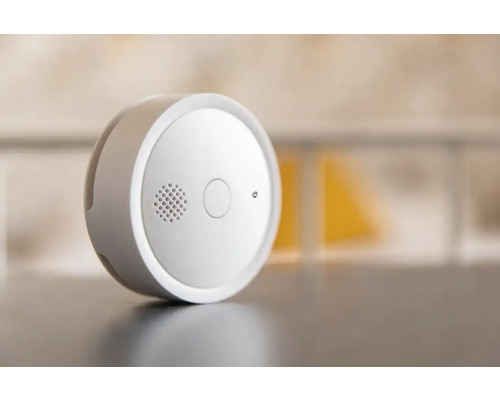 Détecteur de fumée rond avec bouton de test et grille de haut-parleur.