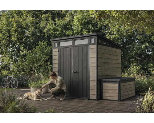 Gartenszene mit Gerätehaus und Truhe, Mann streichelt Hund