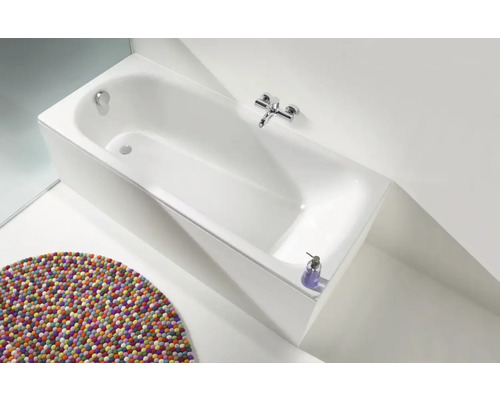 Baignoire rectangulaire avec robinetterie et tapis rond dans la salle de bain.