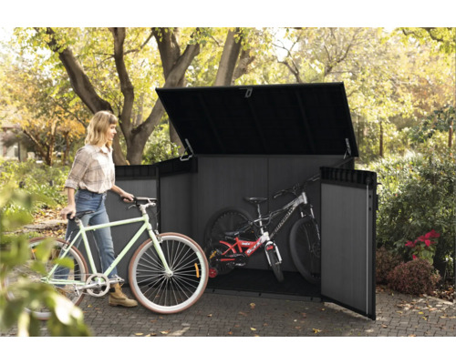 Frau schiebt Fahrrad in Gerätehaus mit Fahrrädern im Garten