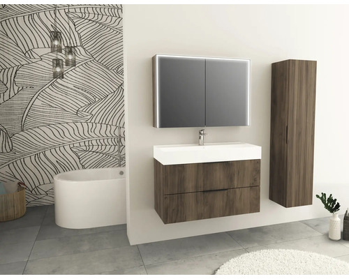 Salle de bains avec meuble-lavabo, armoire de toilette, armoire haute et baignoire devant un papier peint à motifs