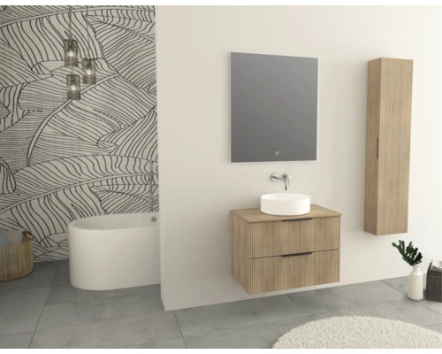Salle de bains avec baignoire, meuble-lavabo, miroir et armoire suspendue en décor bois clair devant un papier peint à motifs de feuilles.