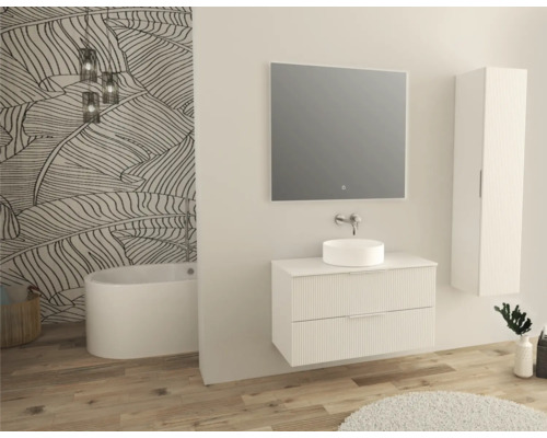 Salle de bains lumineuse avec meuble sous-lavabo, vasque à poser, miroir, armoire haute et baignoire devant un mur à motifs