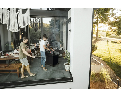 Des personnes font des grillades sur la terrasse avec un barbecue et des meubles de jardin