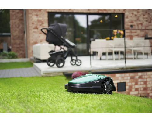 Robot tondeuse sur une pelouse, avec une poussette et une maison en arrière-plan.
