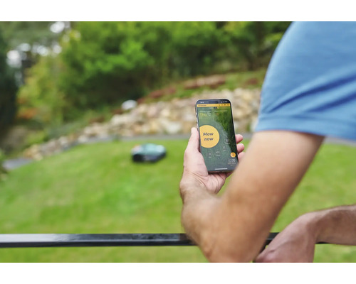 Un homme contrôle un robot tondeuse avec une application pour smartphone