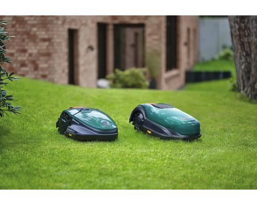 Deux robots tondeuses sur une pelouse devant une maison.