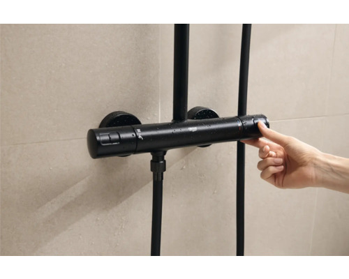 Thermostat de douche noir manipulé d''une main devant un mur carrelé