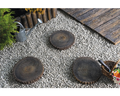 Gartenszene mit Kies, Baumscheiben als Trittsteine, Holzbord, Gießkanne und Korb