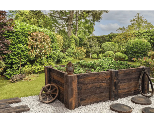 Jardinière surélevée en bois dans le jardin avec des éléments décoratifs tels qu''une roue de chariot et une vieille lanterne