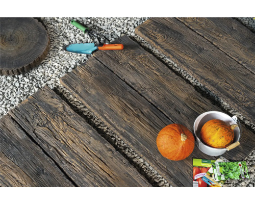 Gartenweg mit Trittplatten in Holzoptik, Kies, Kürbissen und Gartengeräten.